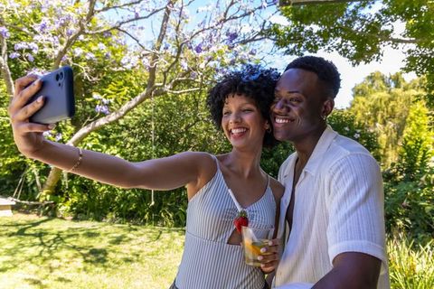 African american couple taking selfie in sunny backyard garden with blooming jacaranda