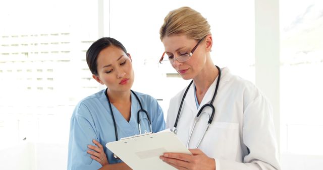 Two medical workers looking over a file and looking at camera at the hospital - Download Free Stock Photos Pikwizard.com
