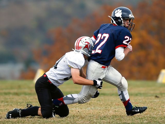 High school football players are playing on a grassy field in autumn. The runner is trying to escape the tackle. Suitable for use in articles about youth sports, athletics, physical education, high school events, or teamwork. Great for promoting sports programs and community events.