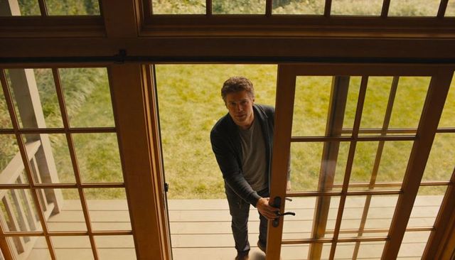 Man opening wooden french doors onto backyard deck, standing on porch, looking inside