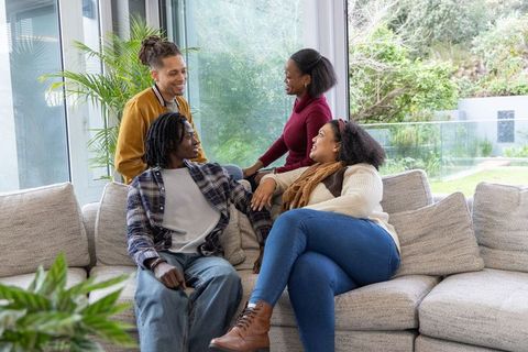 Diverse friends chatting on sectional sofa in modern living room with large windows