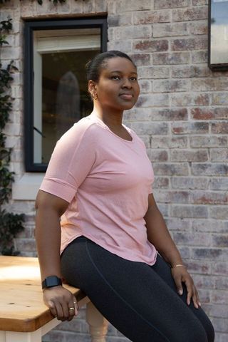 African american woman sitting relaxed on patio bench wearing pink top and smartwatch