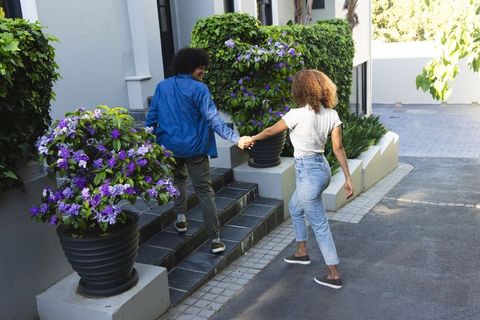 African american couple holding hands walking up steps to modern home with purple flowers