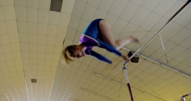 Female gymnast executing a skilled high bar routine in an indoor gymnasium. Perfect for content related to sports, gymnastics competitions, athleticism, training, and physical fitness. Can also be used for promoting gymnastics events, fitness classes, or inspirational sporting achievements.