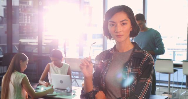 Confident Young Woman Holding Glasses in Modern Office - Download Free Stock Images Pikwizard.com