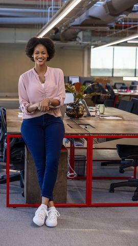 Confident african american woman leaning on communal desk in modern open office