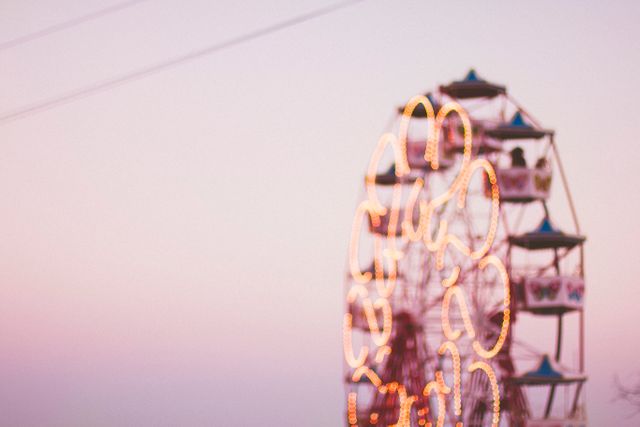 Ferris wheel glowing against pink sky at dusk, shot slightly out of focus, creating a dreamy atmosphere. Ideal for themes related to leisure, amusement parks, and serene evening scenes as a creative background for various projects.
