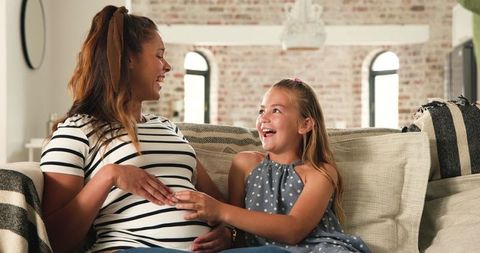 Pregnant woman laughing with daughter on cozy couch