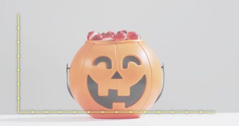 Smiling jack-o-lantern bucket holding red candies on white tabletop for Halloween treats