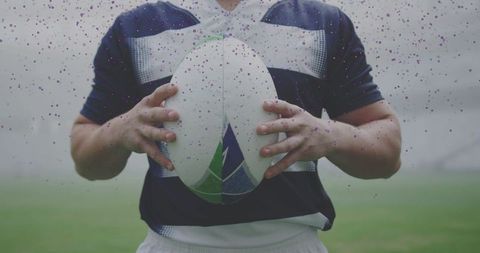 Rugby player gripping ball with both hands on misty grass pitch showing focus and determination