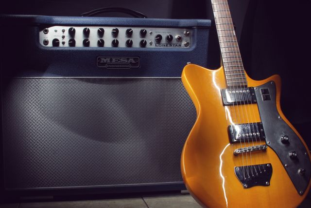 Vivid orange electric guitar leaning against a large amplifier in a music studio. Ideal image for music-related articles, blogs about musical instruments, advertisements for guitar or amplifier sales, or videos about learning to play the guitar. The setup conveys a sense of musical passion and professional equipment.
