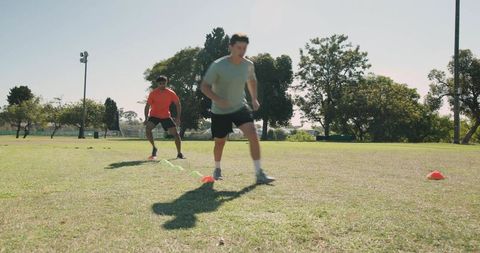 Diverse male athletes performing agility cone drills on grassy field for speed training