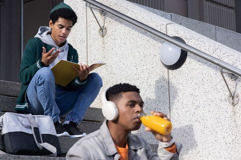 African american students studying on campus steps drinking juice and listening to music