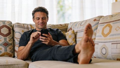 Relaxing man reclining on patterned sofa browsing smartphone, enjoying home lifestyle