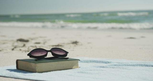 Sunglasses and book on beach towel at sunny beach, copy space. Vacations, summer, free time and relaxation.