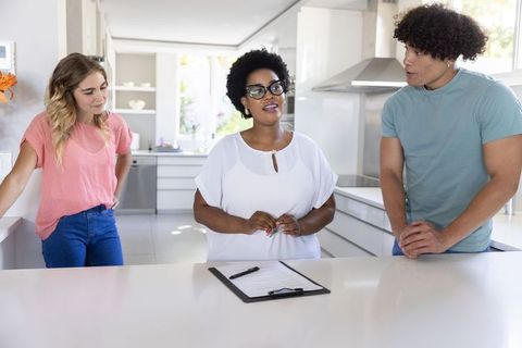 Black woman advisor explaining contract to young couple in modern kitchen consultation