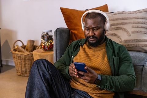 African american man relaxing with headphones and smartphone on cozy living room floor