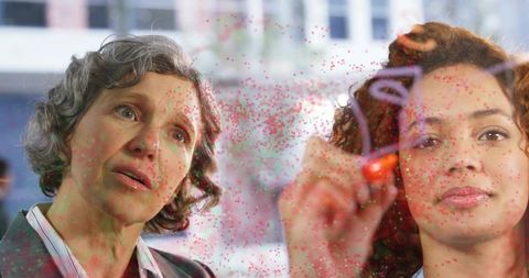 Businesswomen Brainstorming Ideas on Glass Panel with Diagrams