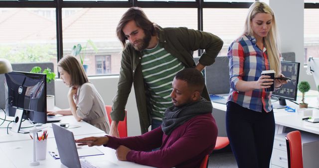 Diverse group of colleagues working together on project tasks in a modern office. One person is pointing at laptop screen while others are engaged in discussion and holding documents. Perfect for business, workplace diversity, teamwork, workplace collaboration, and modern office concepts.