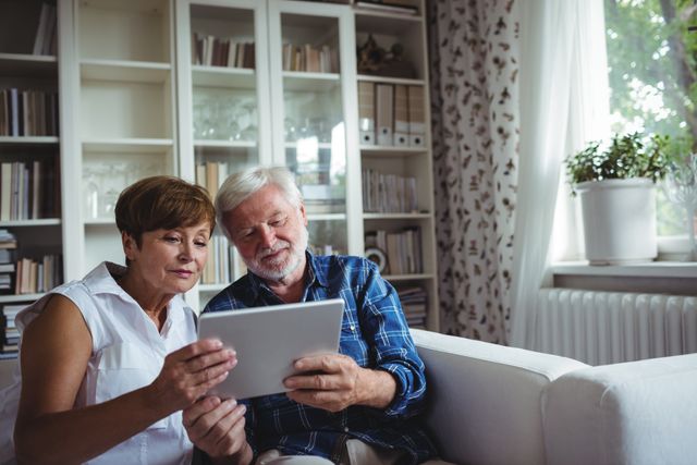 Senior couple sitting on sofa and using digital tablet in living room