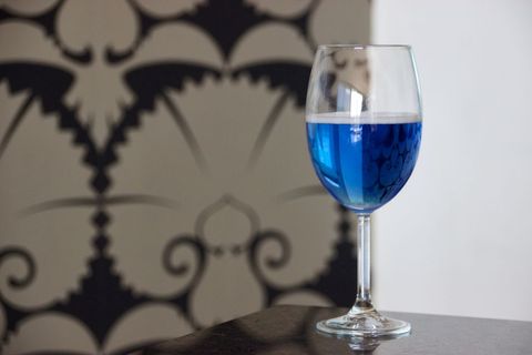 Elegant glass with blue liquid against sophisticated patterned wall