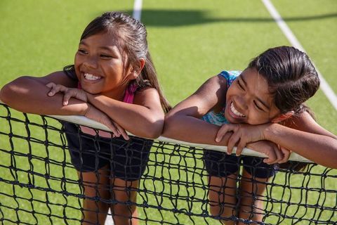 Smiling girls leaning on tennis net in outdoor sunshine