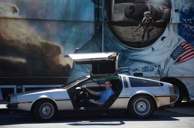 Perfect for projects involving retro cars, sci-fi themes, and popular culture references. The DeLorean DMC-12, featured here with its distinctive gull-wing doors, parked against an astronaut mural background, commemorates 'Back to the Future' iconic time machine. Useful for designs about nostalgia, vintage cars, or NASA-related promotions.