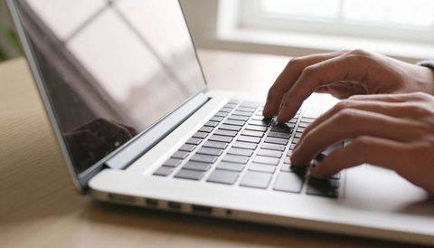 Hands Typing on Laptop Keyboard Close-up in Home Office Workspace with Natural Light