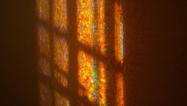 Orange and yellow mosaic window casting light on wall