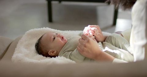 Diverse mother cradling baby on plush blanket embraces tender comfort