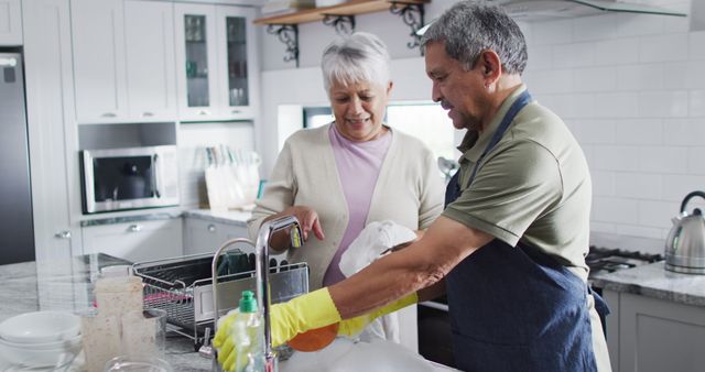 Happy senior biracial couple washing dishes in kitchen. Spending quality time at home, retirement and lifestyle concept.