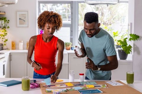 African american couple planning wellness routine on corkboard in bright home kitchen