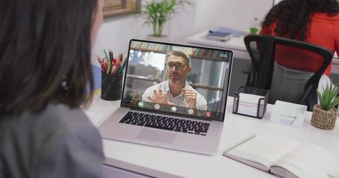 Woman watching remote video call with male colleague on laptop at coworking office desk