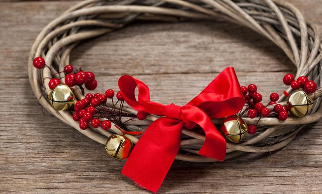 Close-up of a grapevine wreath adorned with a red ribbon and golden bells, placed on a wooden plank. Ideal for use in holiday-themed designs, Christmas cards, festive invitations, or seasonal marketing materials.
