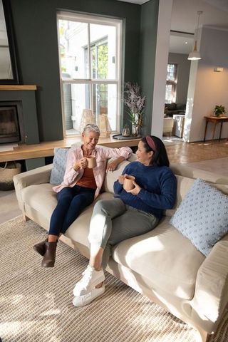 Mature friends sharing coffee and laughter on cozy sofa in bright modern living room