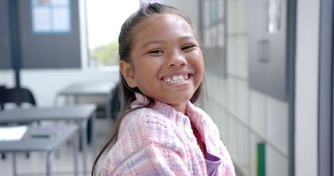 Smiling Schoolgirl in Classroom Wearing Colorful Sweater