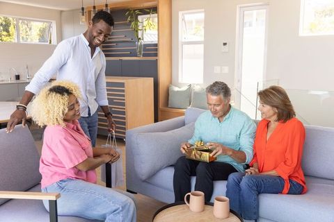 Multigenerational diverse friends celebrating gift opening in modern cozy living room
