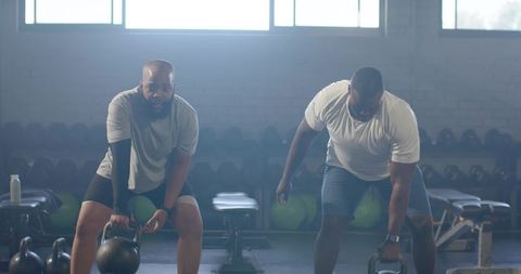 African American Men Lifting Kettlebells in Industrial Gym Partner Strength Training