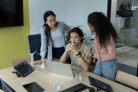 Multiracial team designing renewable energy solutions with solar panels and wind turbines