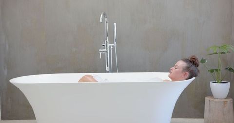 Woman Relaxing in Modern Freestanding Bathtub in Minimalist Bathroom