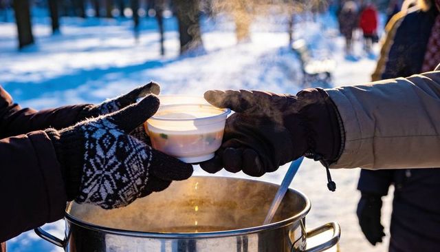 Volunteers handing steaming soup to gloved hands in snowy park during winter outreach