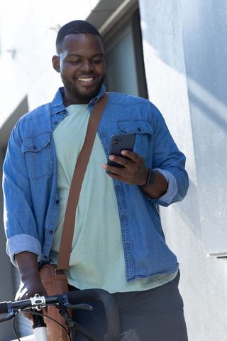 Smiling african american commuter checking smartphone while holding bike in urban denim