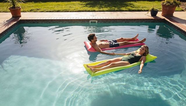 Couple floating on bright inflatable loungers in backyard pool on sunny afternoon