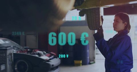 Asian Mechanic Repairing Car Wheel with Currency Overlays