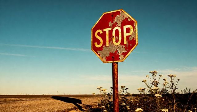 Rusting Stop Sign Peeling Paint Casting Long Shadow on Rural Road at Golden Hour