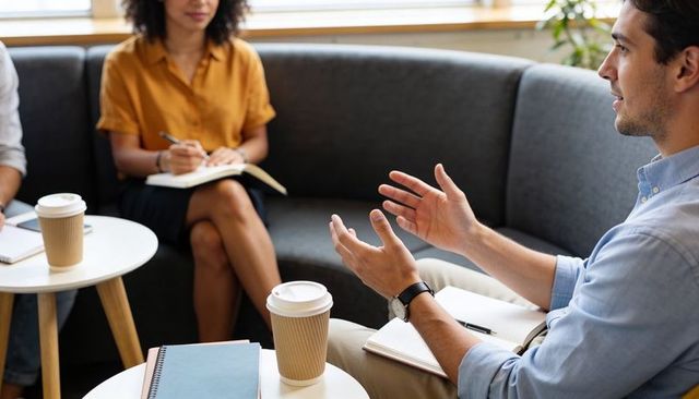 Team collaborating in modern office lounge, man gesturing, colleagues taking notes