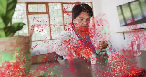 Senior indian woman reaching for eyeglasses at table with red-green particle overlay home