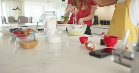 Mixing batter on sunlit marble kitchen island, home baking with flour jar and fruit