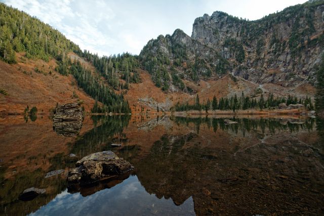 Calm mountain lake with reflections of the surrounding rocky landscape and pine trees. Ideal for nature, outdoor, and landscape photography websites or travel brochures highlighting natural beauty and serene locations.