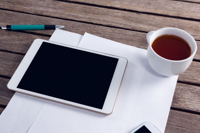 Digital tablet, cup of black coffee, and blank paper on wooden table create a modern workspace setup. Ideal for illustrating concepts of productivity, remote work, planning, and business environments. Suitable for use in articles, blogs, and advertisements related to technology, office work, and modern workspaces.